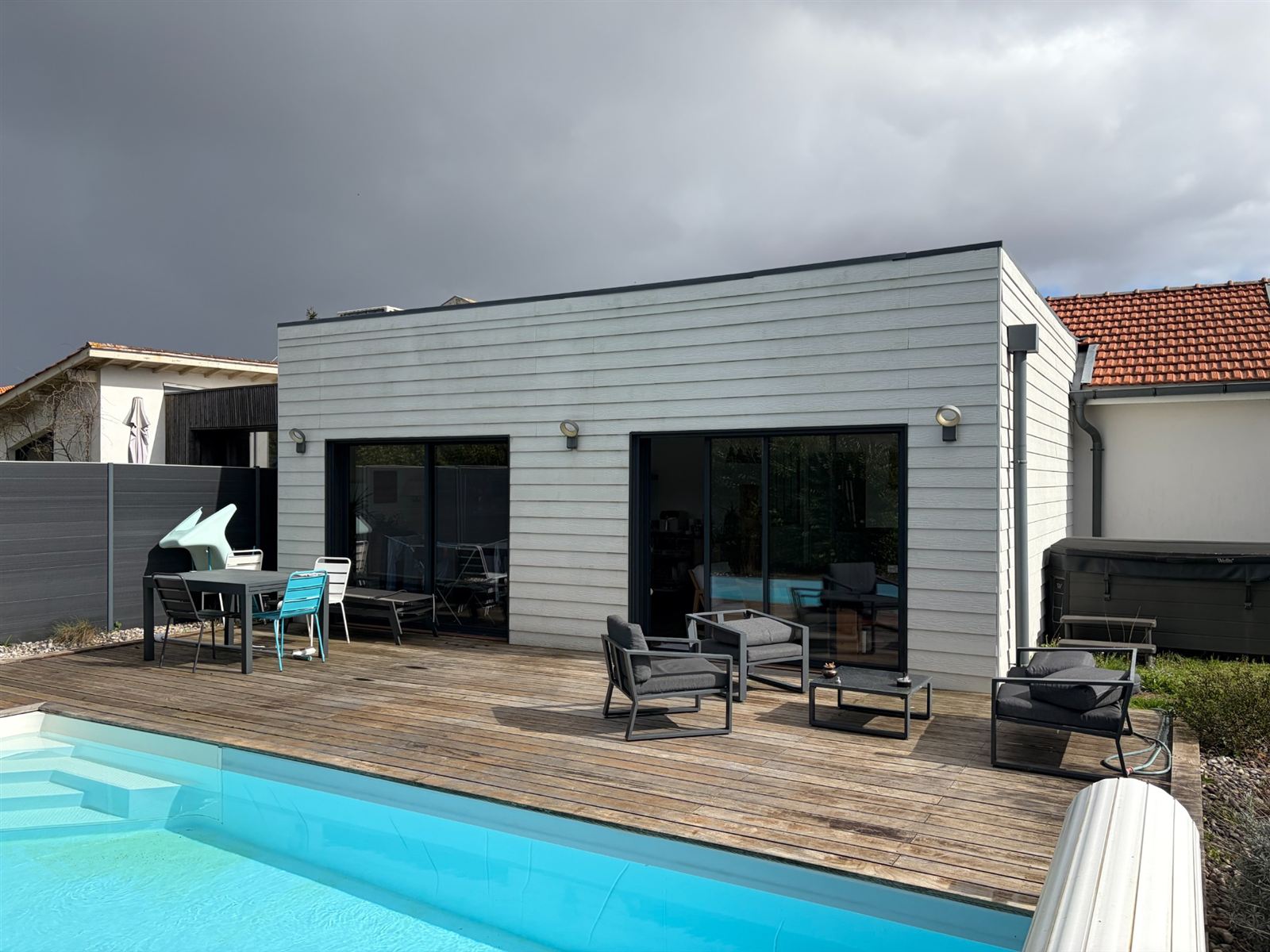 Avant : Terrasse de piscine sans protection équipée de deux stores bannes toile beige déployés, sur la photo réelle du client